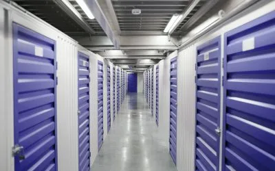Clean, indoor self-storage facility hallway lined with secure green metal units. Affordable and reliable storage services in Sharjah by dxbmovershub.com.