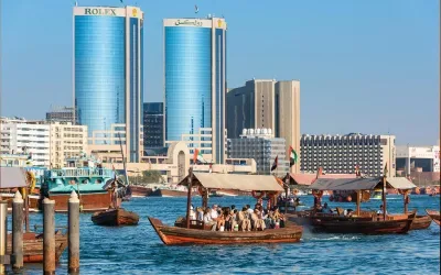 Traditional wooden boats (Abras) carrying passengers across the water with modern twin skyscrapers in the background of Bur Dubai. Local moving services for residents and businesses in Bur Dubai by dxbmovershub.com.