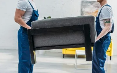 Two professional movers from dxbmovershub.com carrying a sofa, demonstrating our heavy furniture handling services for commercial clients.
